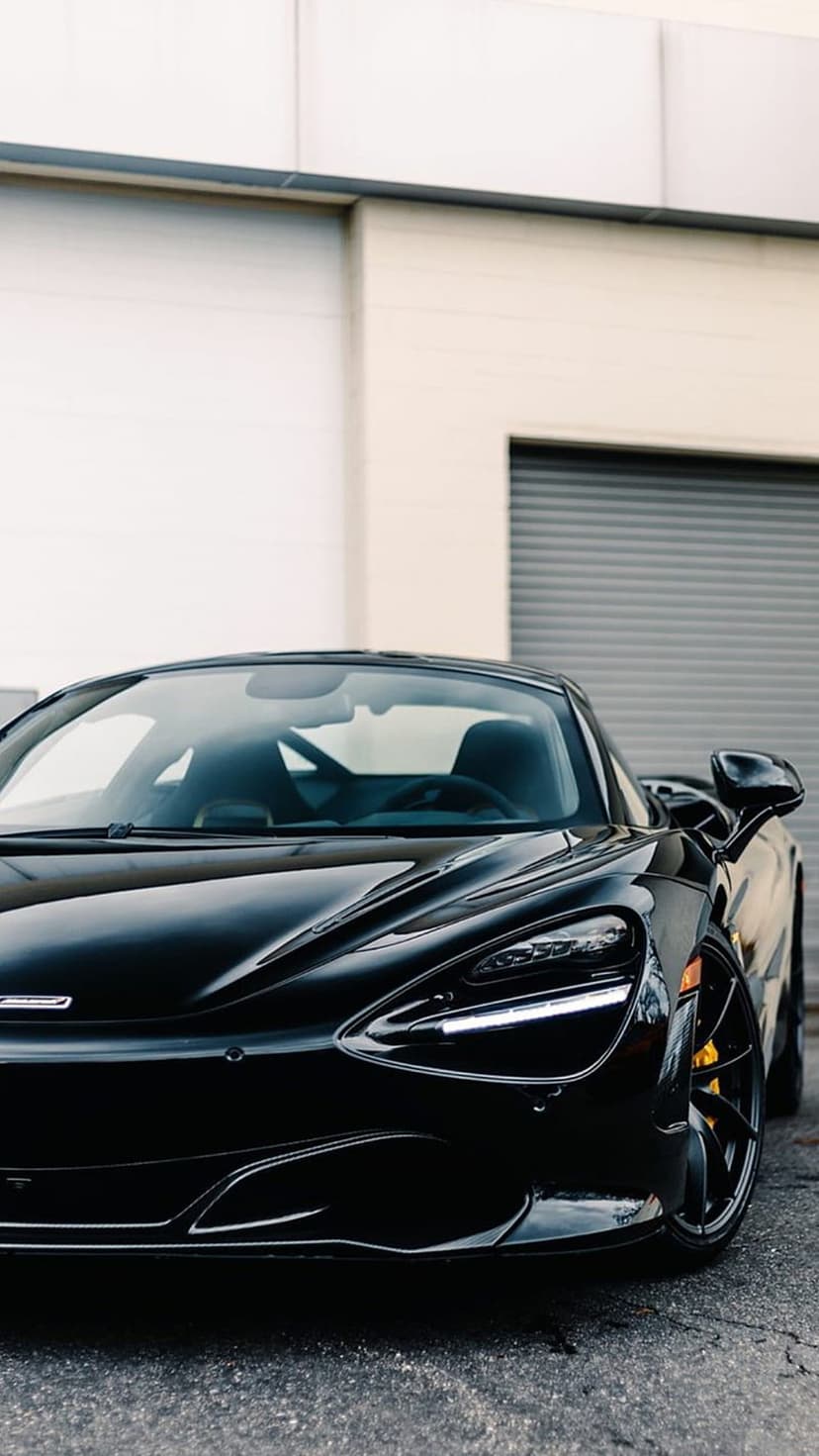 McLaren 720S supercar in glossy black features yellow brake calipers and sharp LED headlights at a low angle.