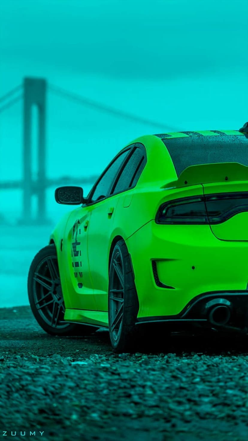 Bright green Dodge Charger rear view parked on dark pavement under a large bridge during a cyan twilight.