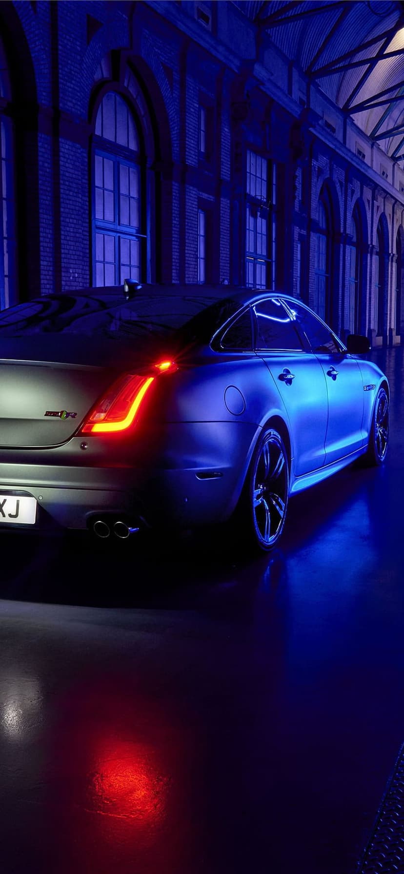 Jaguar XJR rear exterior viewed from a low angle under vibrant red and blue neon lights against brick arches.