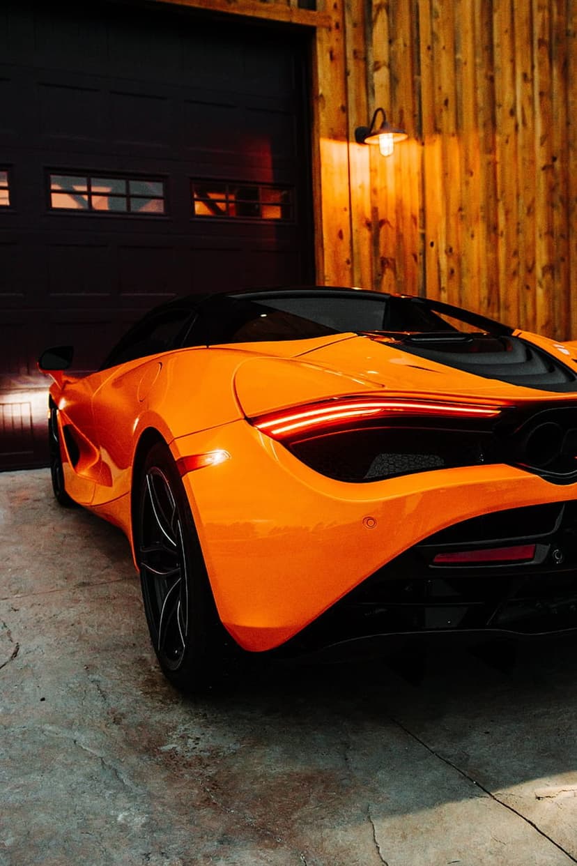 McLaren 720S with glowing taillights parked on a concrete garage floor beside a dark wooden wall.