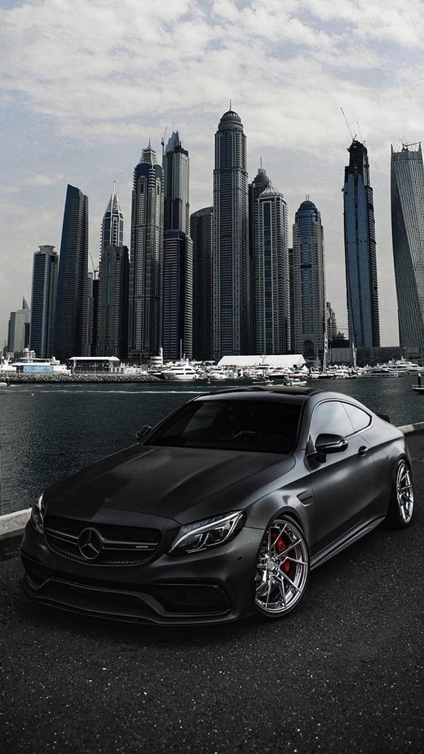 Matte black luxury coupe parked overlooking the Dubai Marina skyline and illuminated skyscrapers during twilight.