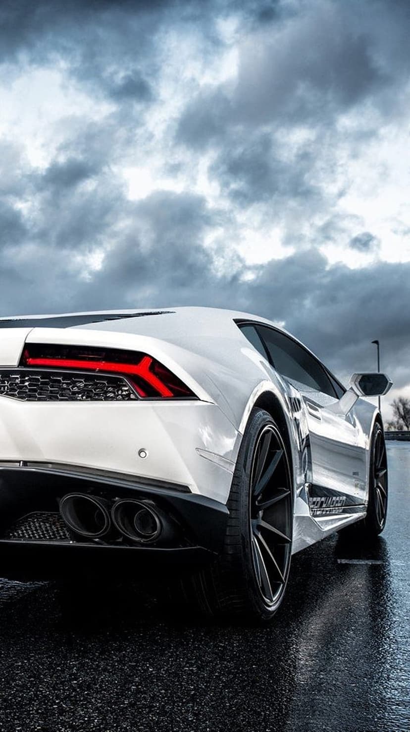 White Lamborghini Hurricane rear view parked on wet asphalt beneath a dark, stormy sky with glowing taillights.
