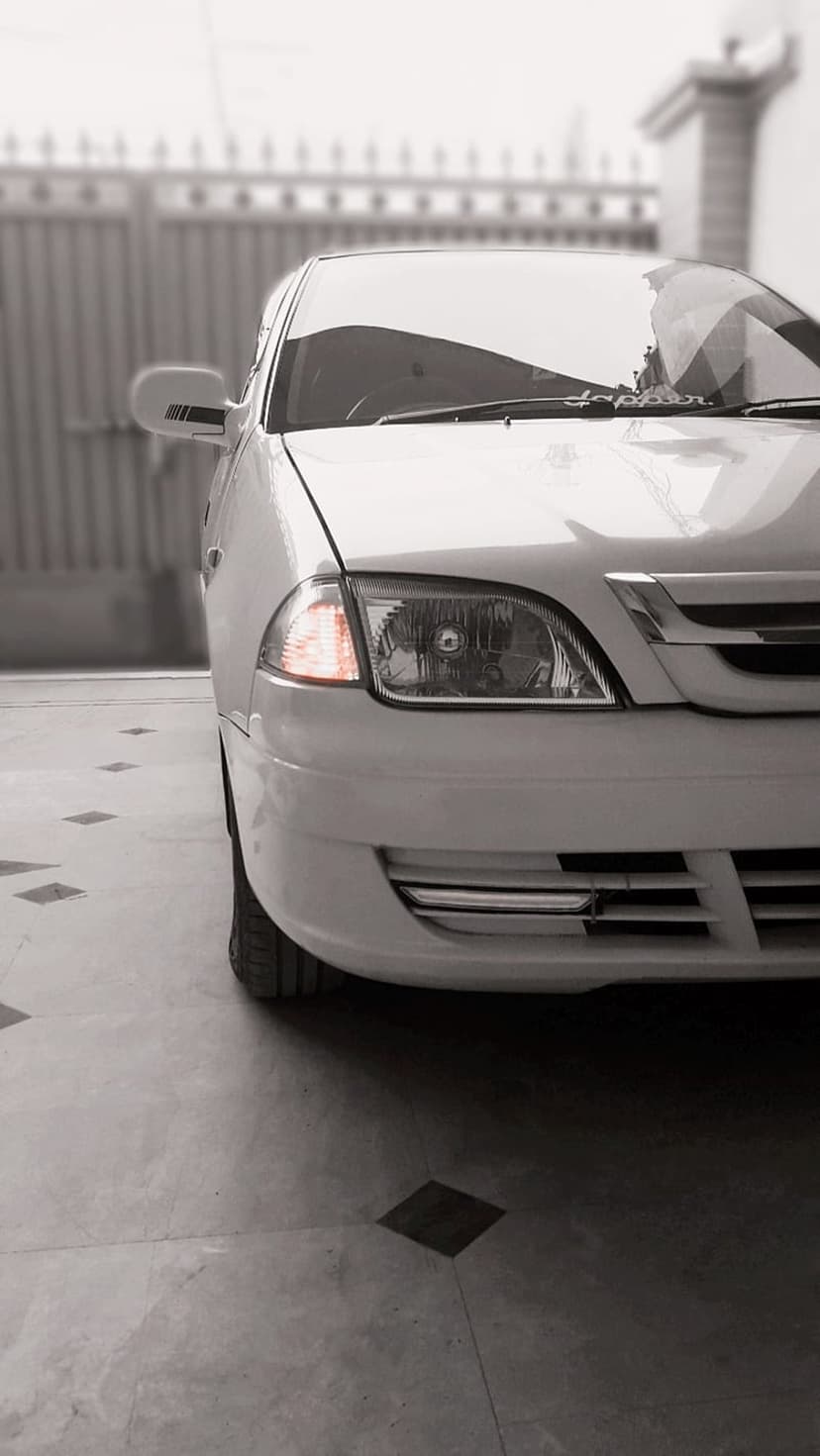 White car front corner featuring a chrome grille, glowing amber signal, and tire on a monochrome tiled floor.