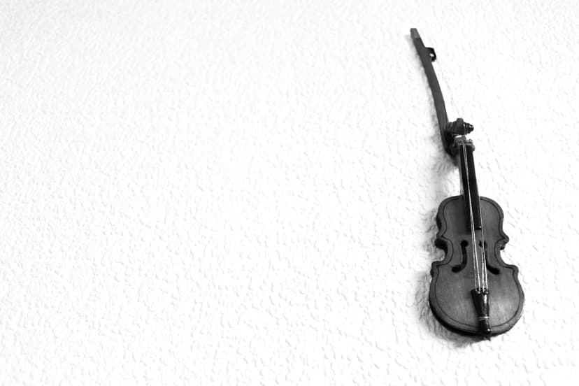 Vintage violin suspended vertically on a heavily textured white wall with deep shadows and negative space.