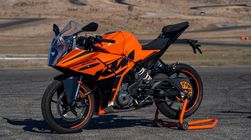 Orange KTM RC 390 sportbike on a rear paddock stand parked on an asphalt racetrack under clear bright daylight.