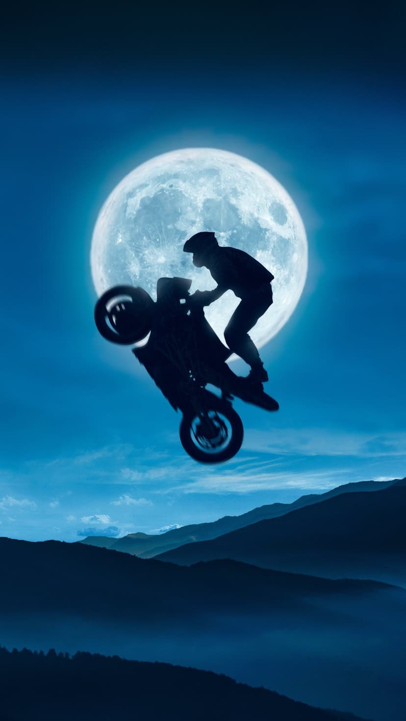 Motorcyclist performing a wheelie silhouette against a giant glowing full moon and misty mountain peaks at night.