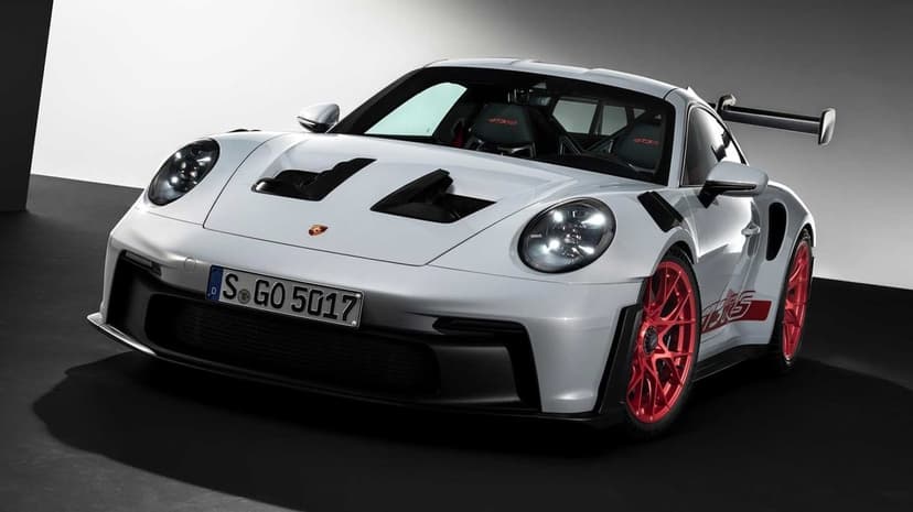 White Porsche 911 GT3 RS sports car with red wheels and large rear wing in a minimalist studio setting.