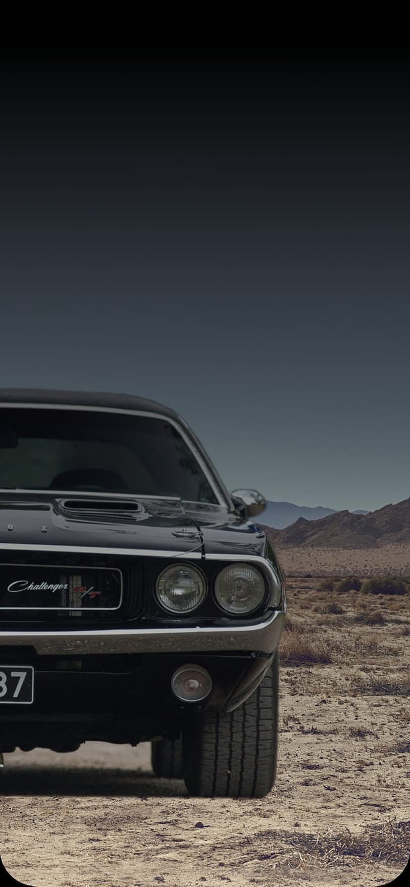 Dark blue vintage Dodge Challenger parked on a dry desert plain with rocky mountains in the far distance.