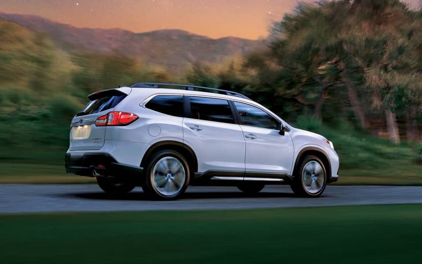White SUV driving on a road with motion blurred wheels against a mountain sunset and soft twilight sky.
