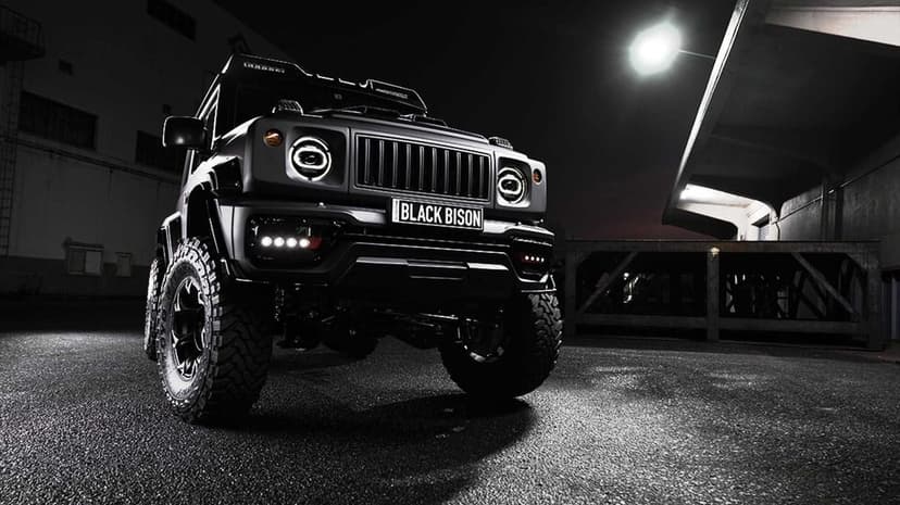 Matte black off-road vehicle with illuminated LED headlights parked on dark asphalt under a bright night light.
