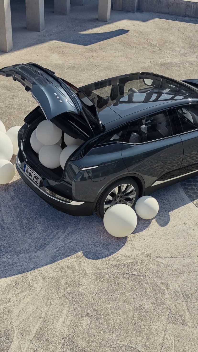 Dark gray SUV with open trunk filled with large white spheres on a sunlit concrete surface.