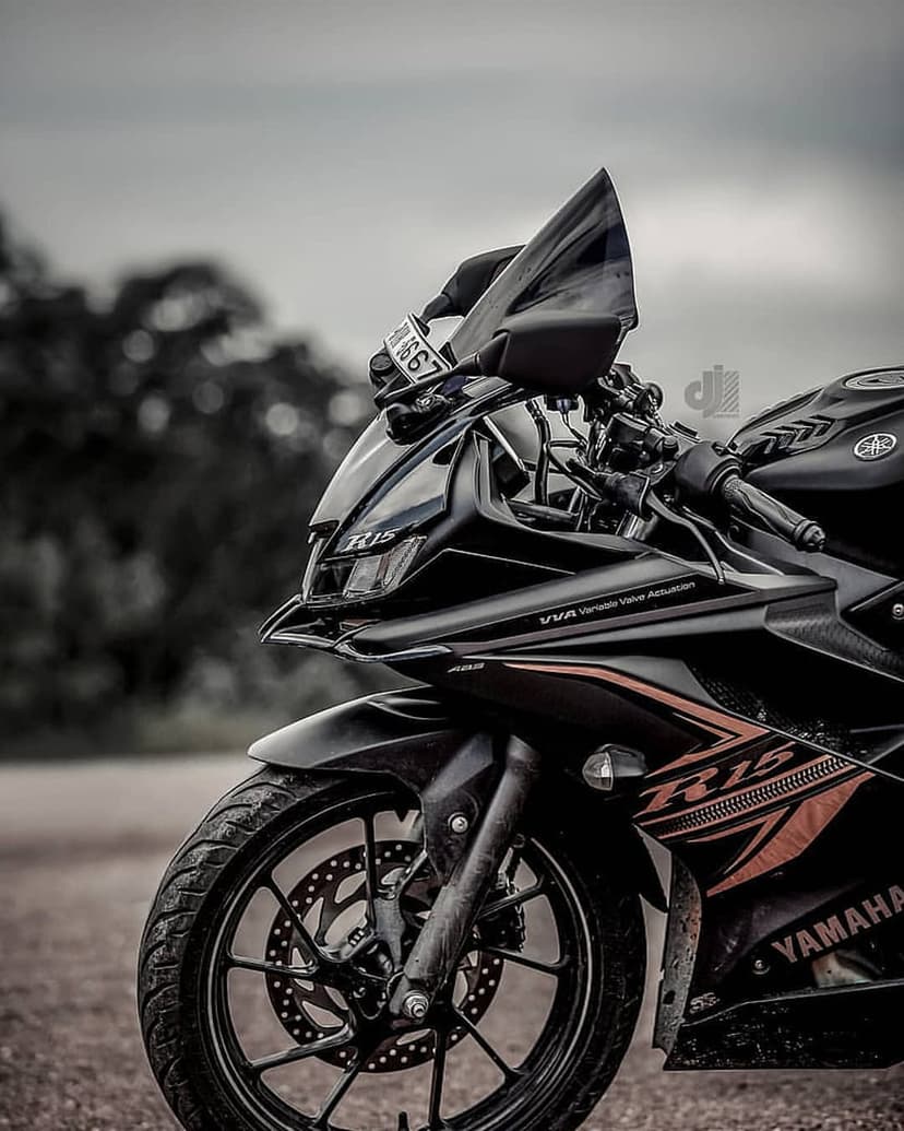 Yamaha R15 motorcycle front wheel and brake disc on a matte black fairing with silver branding against trees.