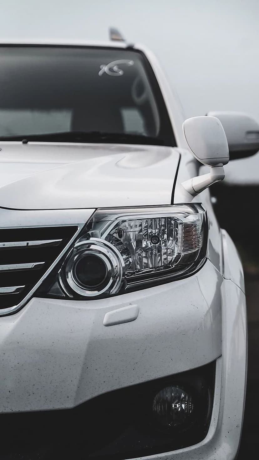 White SUV headlight with intricate LED details and a chrome textured grille captured from a low-angle perspective.