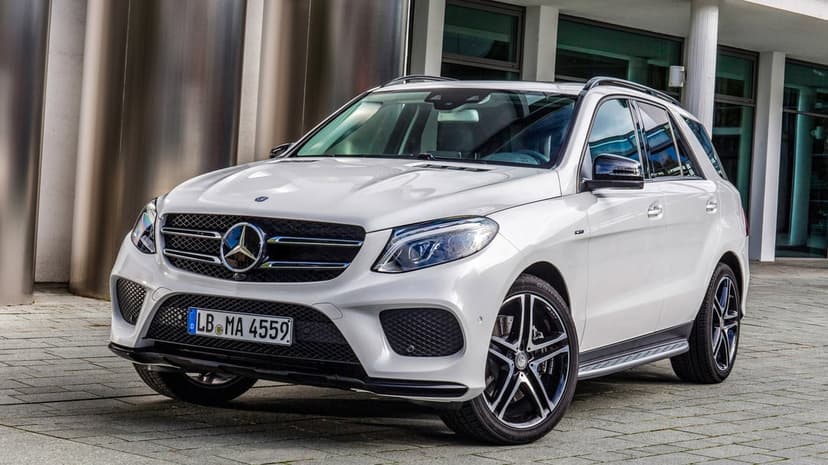 White Mercedes-Benz GLE SUV with alloy wheels parked on pavement in front of a modern glass office building.