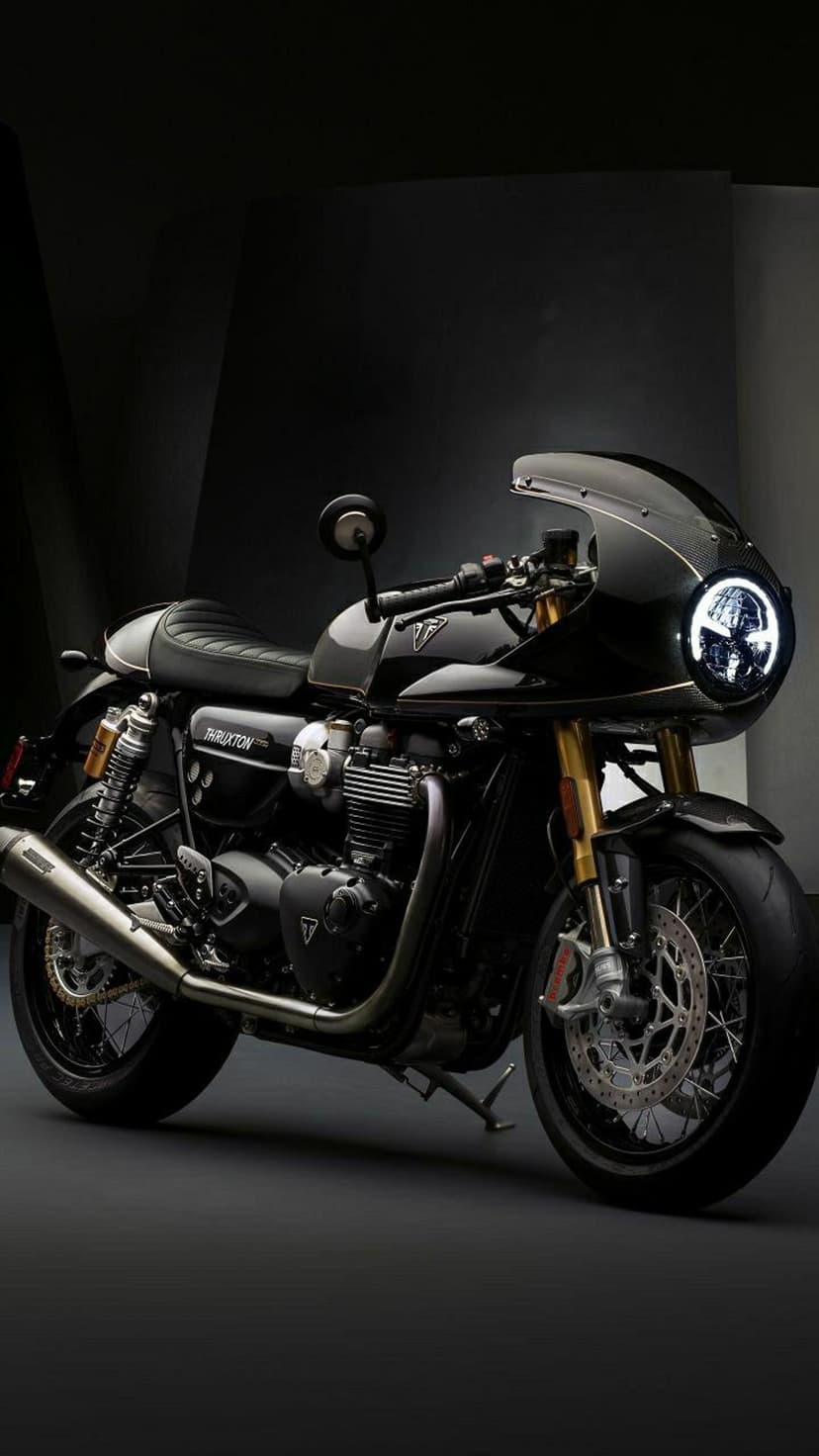 Triumph Thruxton R motorcycle with gold forks and black fairing parked in a dark studio under soft spotlights.