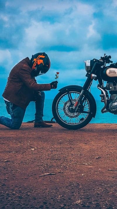 Man Kneels with Rose Beside Motorcycle on Coastal Road