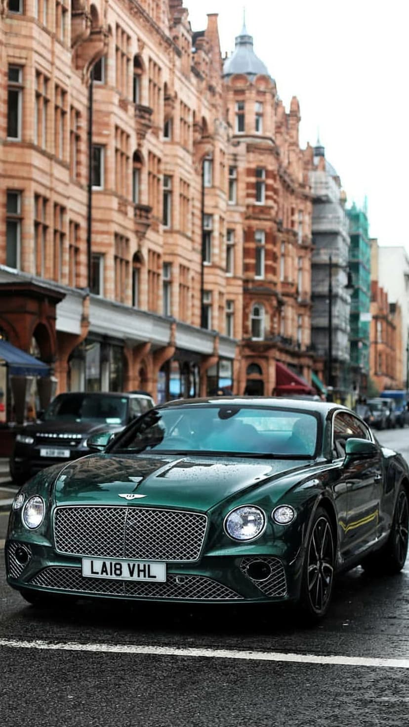 Bentley Continental GT in British Racing Green parked on a damp city road surrounded by classic London buildings.