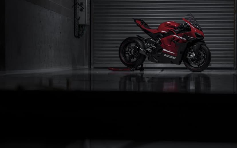 Red Ducati sportbike parked in a dark garage with a corrugated door and reflections on a polished floor.