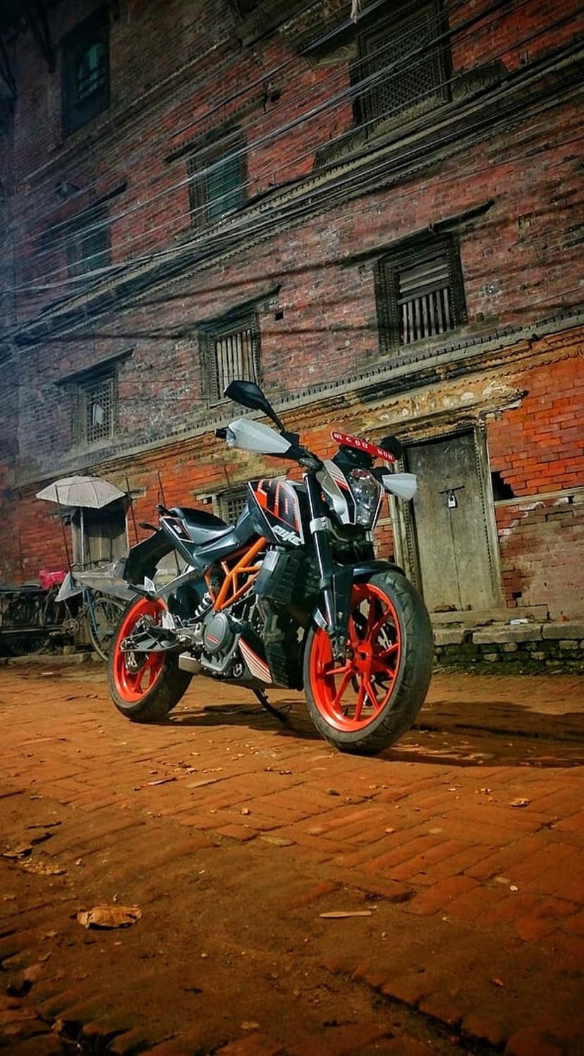 KTM Duke motorcycle with orange wheels parked in a dark brick courtyard in front of an old building at night.