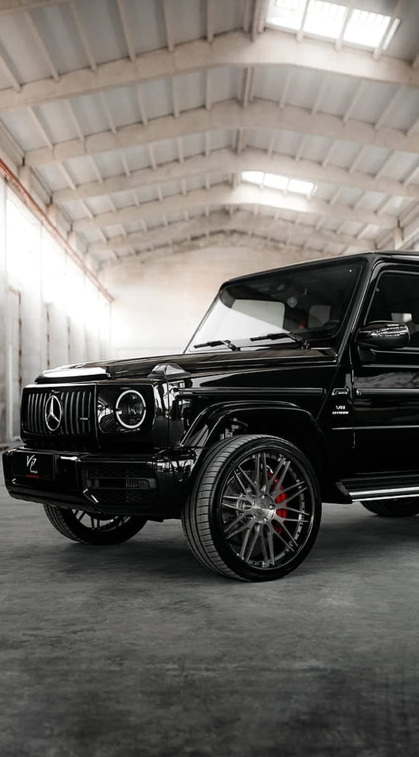 Black Mercedes G-Wagon SUV with custom rims and red brake calipers parked in a dimly lit indoor showroom.
