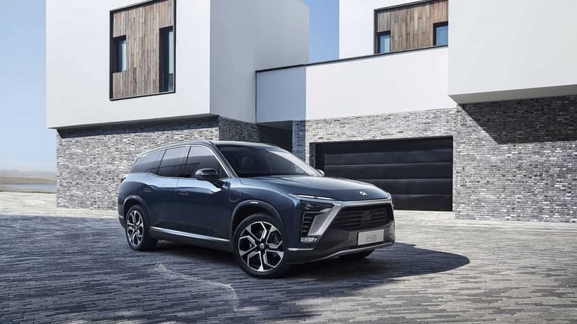 Dark blue NIO ES8 electric SUV parked on grey cobblestones in front of a modern minimalist white building.