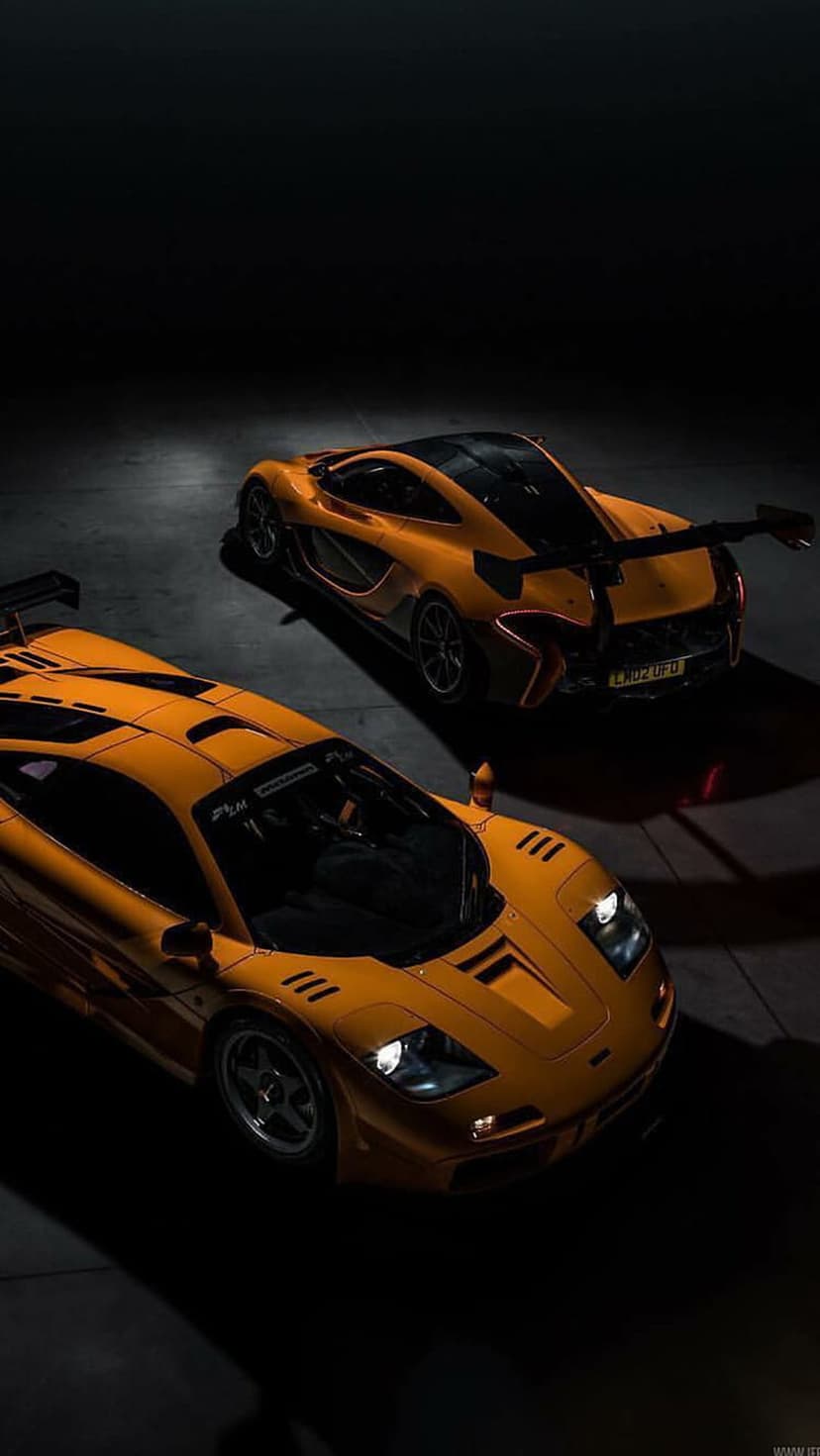 Orange McLaren P1 and F1 supercars parked in a dark studio with soft glowing headlights and sleek bodywork.