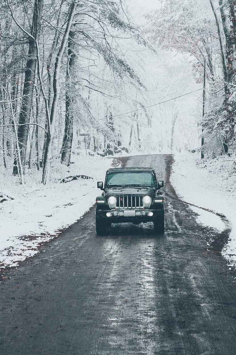 Black Jeep Wrangler driving along a wet, slushy path through a snow-covered forest during a cold winter day.