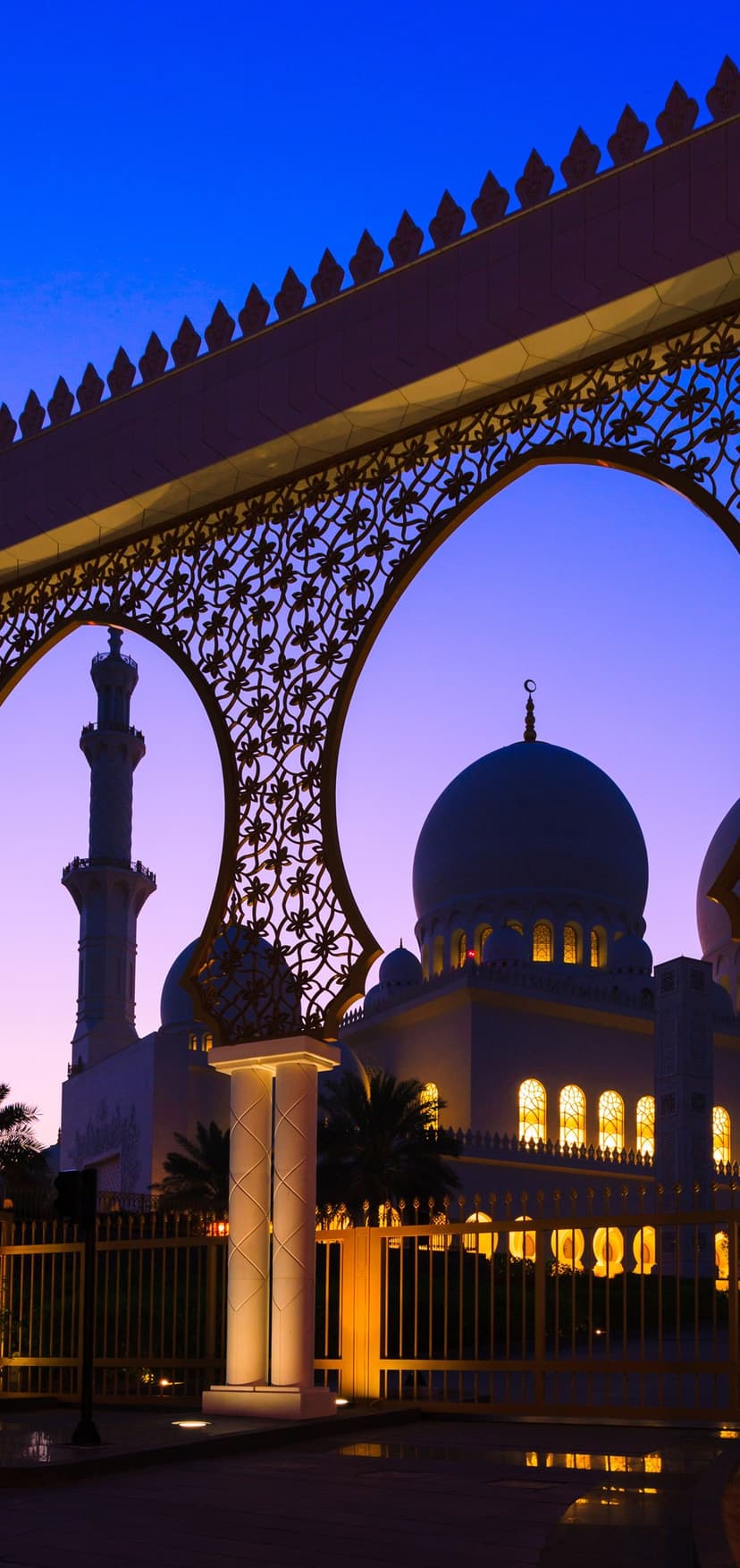 Sheikh Zayed Mosque domes and minarets viewed through a golden archway under a purple and blue sunset sky.