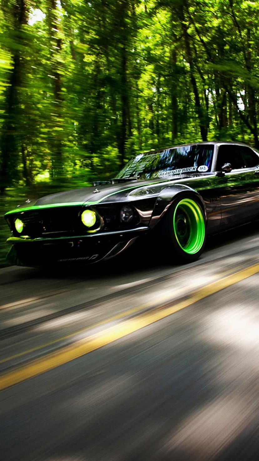 Black Ford Mustang with glowing green wheels speeding past trees with heavy motion blur on a narrow asphalt road.