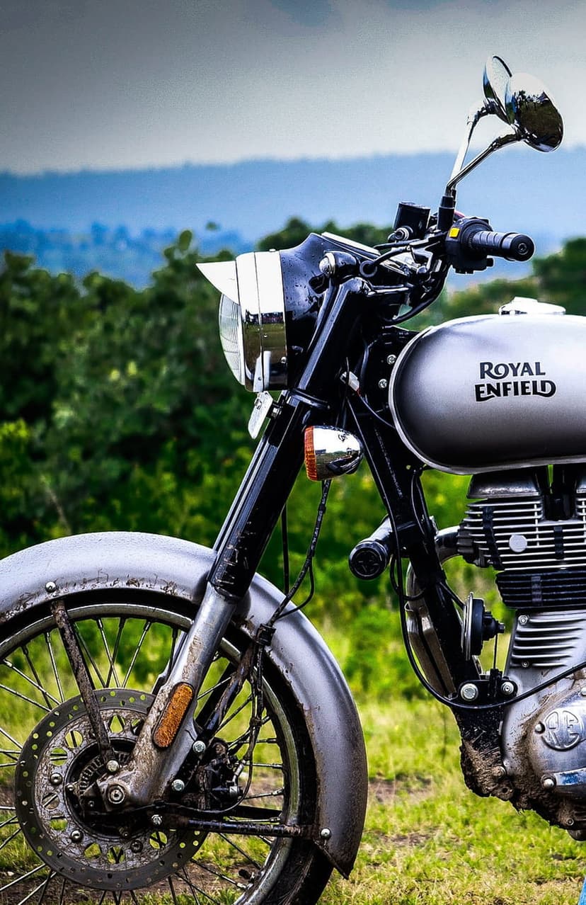 Silver Royal Enfield motorcycle with chrome details parked in a green field under a clear blue sky.