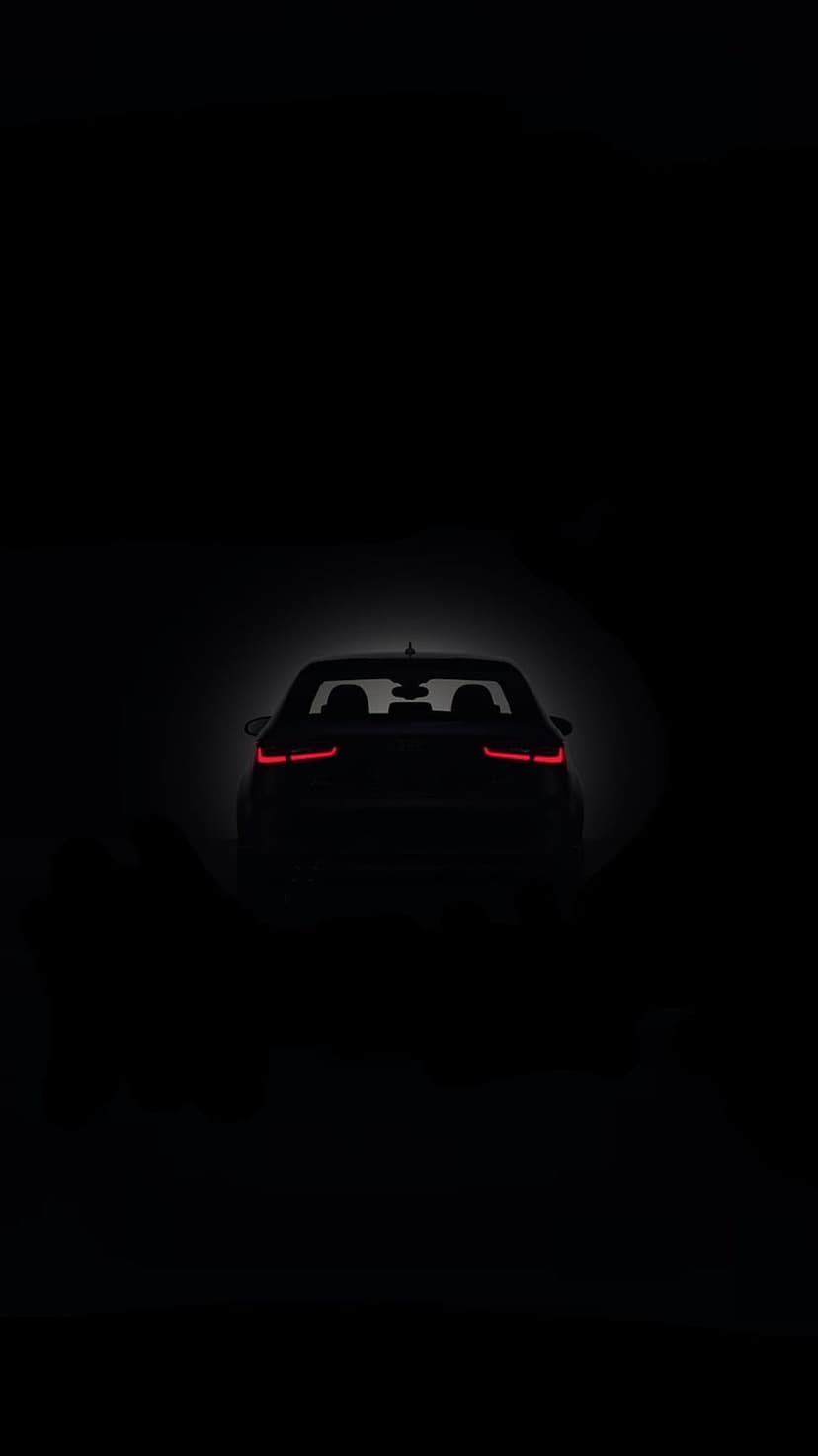 Ruby red taillights glowing on the rear of a dark car silhouette positioned against a solid black background.