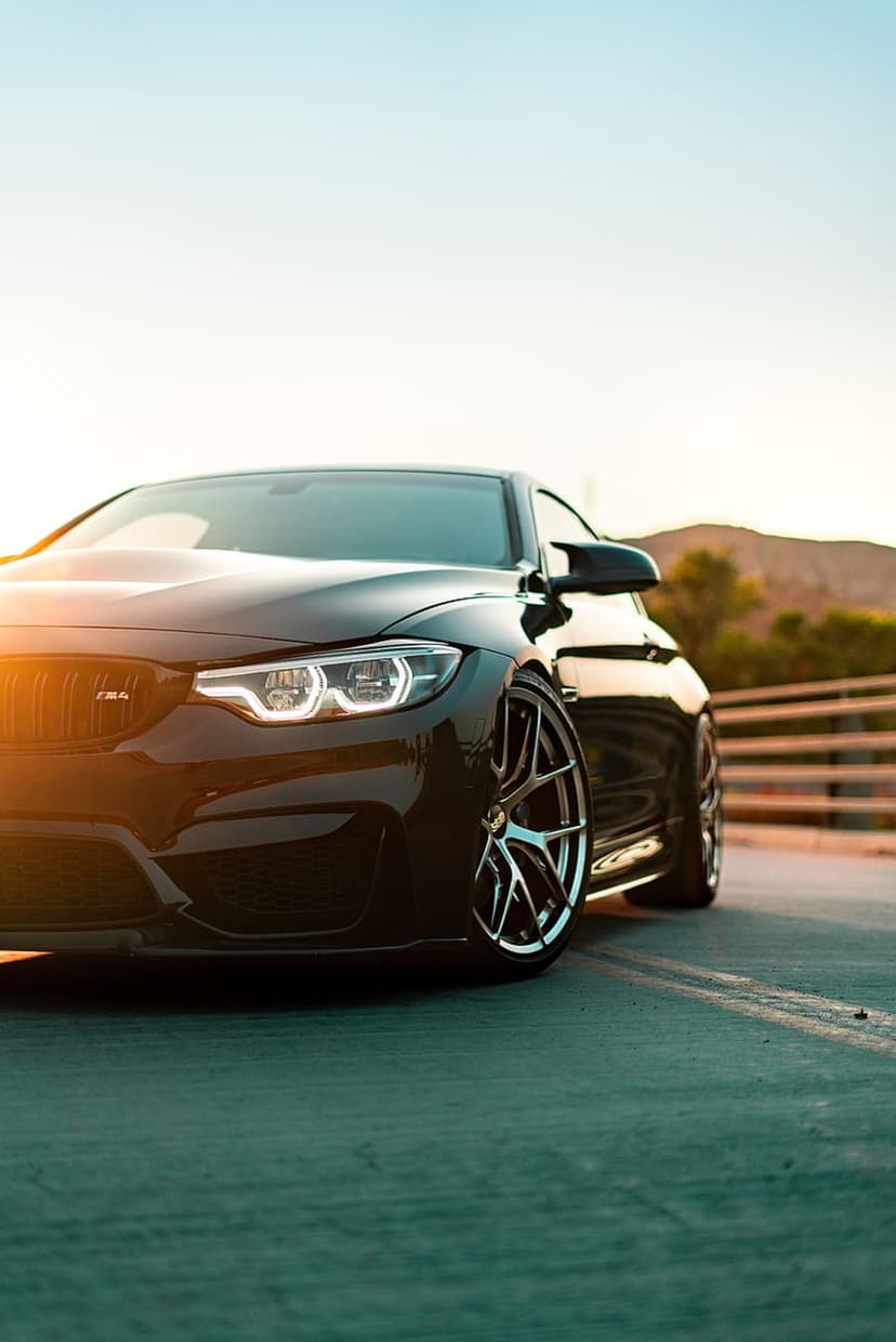 Black BMW M4 sports coupe drives on a paved road during a golden sunset with blurred trees in the background.