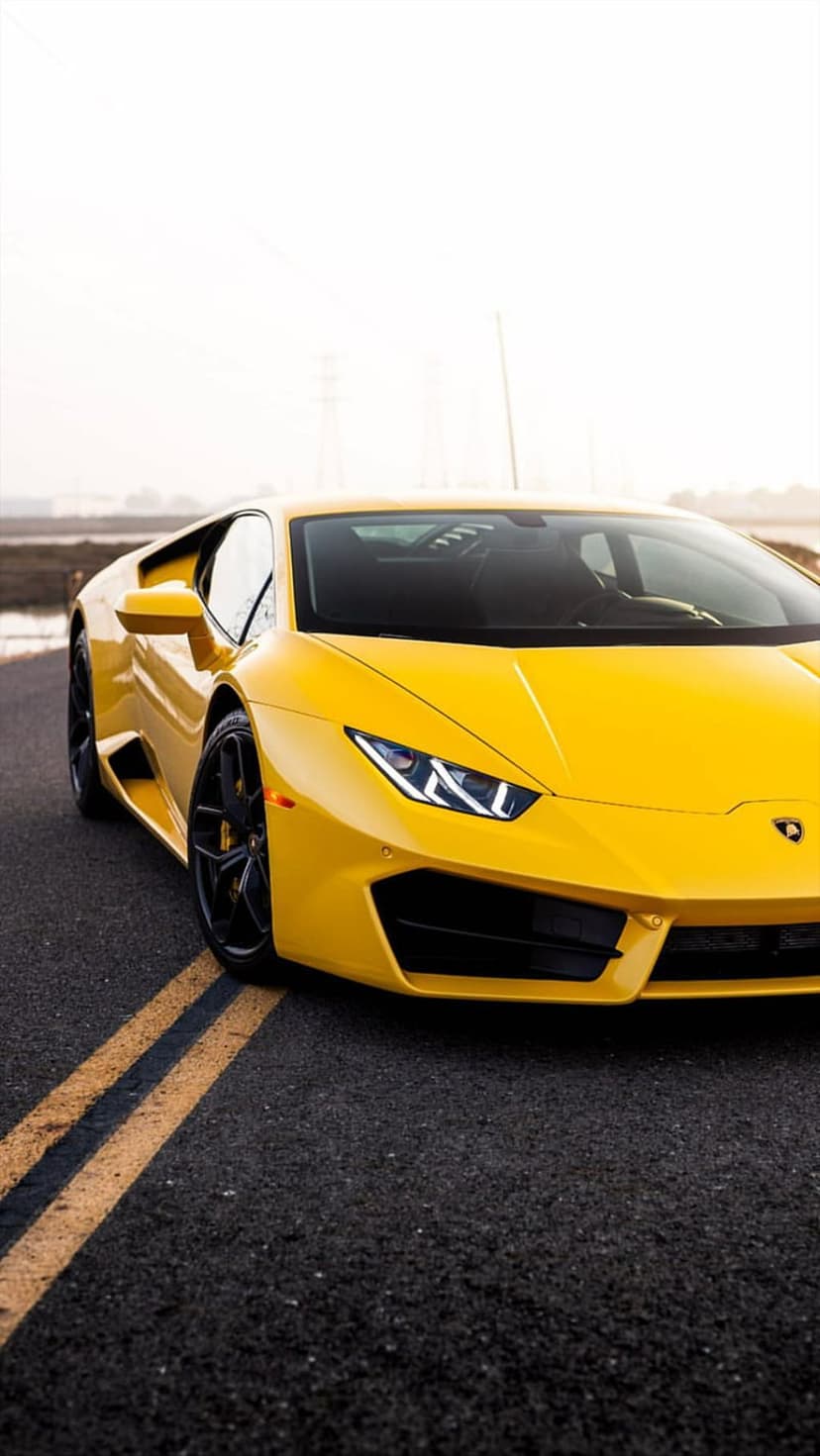 Yellow Lamborghini Huracan driving on a paved road with double yellow lines, captured from a low front-left angle.