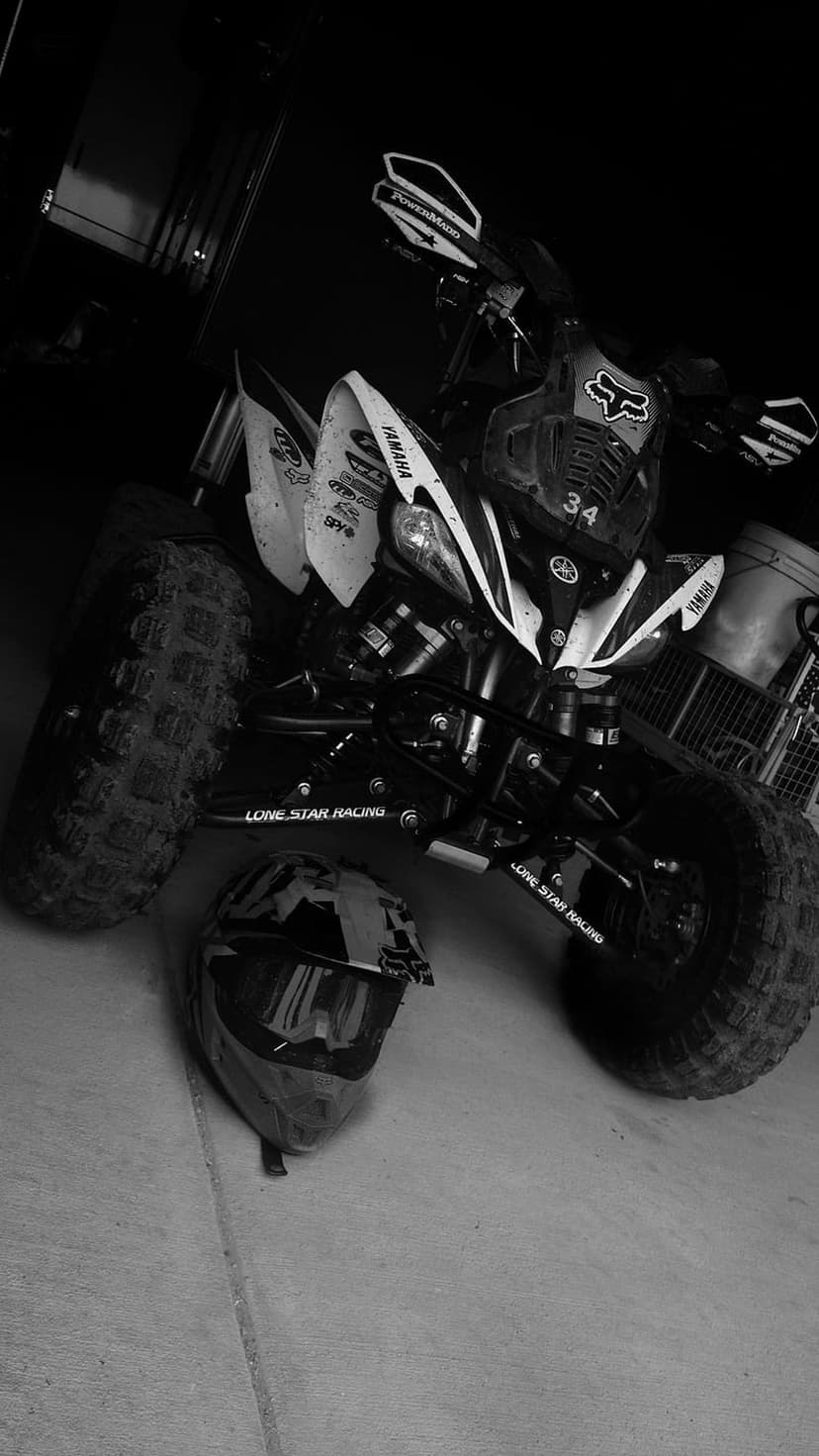 Yamaha ATV and Fox Racing helmet sit on a dark ground with high-contrast lighting in a black and white scene.