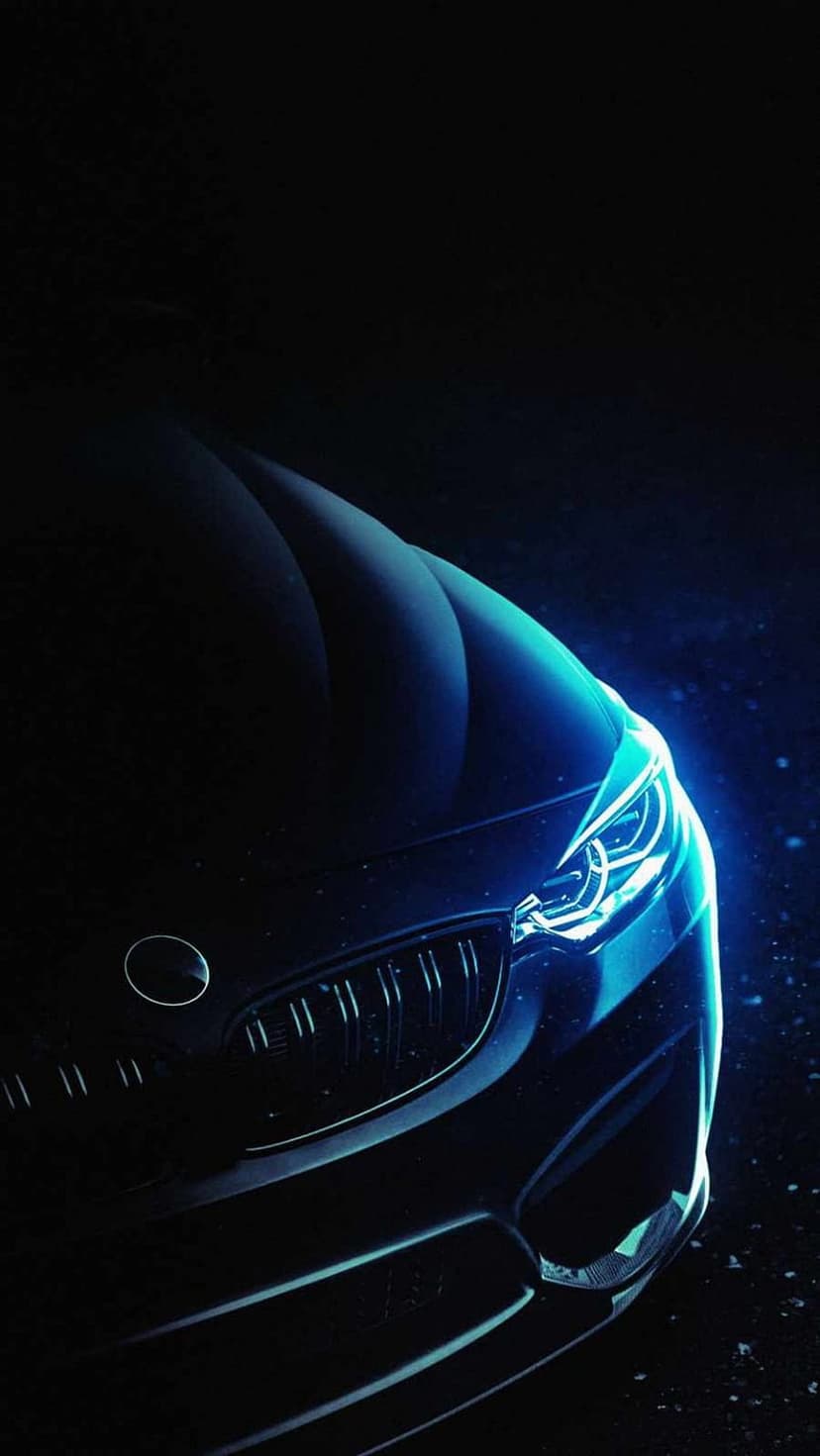 Dark blue BMW M car front end with glowing blue LED headlights and glossy reflections on the hood at night.