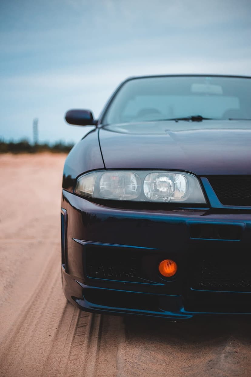 Nissan Skyline R33 front fascia with glowing fog lights on a sandy beach under a clear blue sky in vertical view.