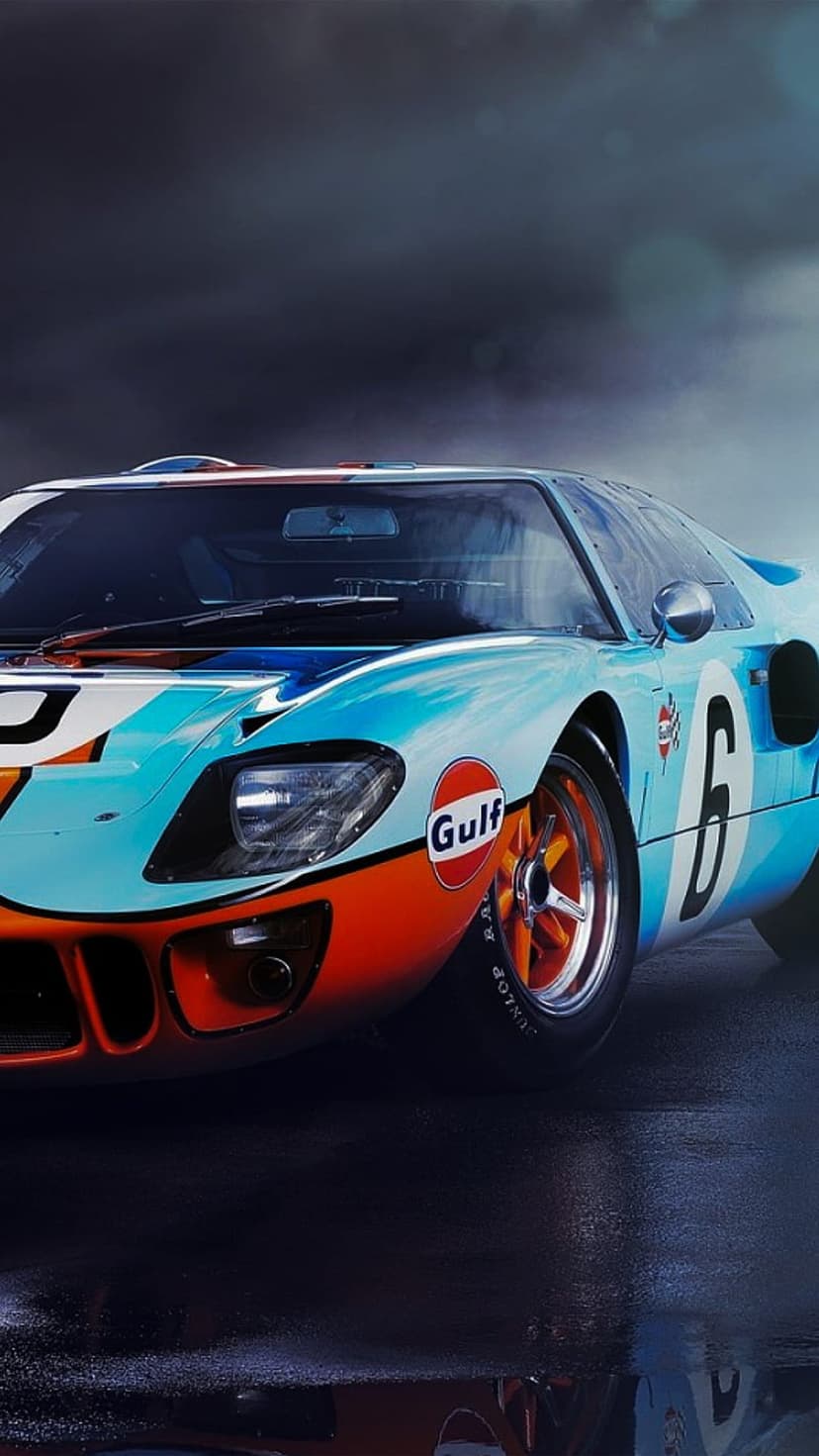 Ford GT40 race car in light blue and orange Gulf colors rests on a glistening wet track with visible number six.