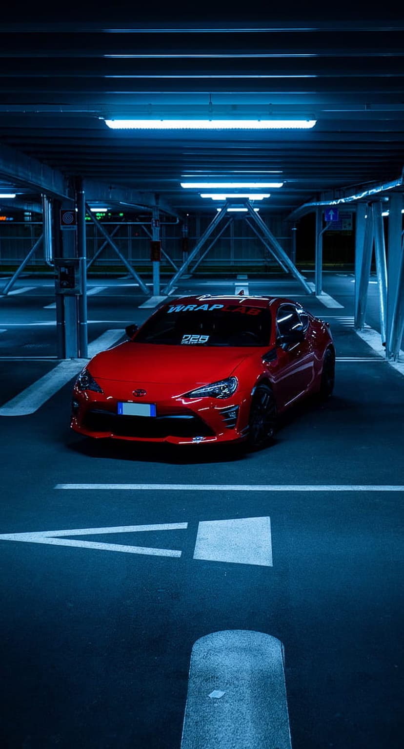 Red Toyota GT86 sports car parked in a blue-lit underground garage with white lines on the dark asphalt floor.