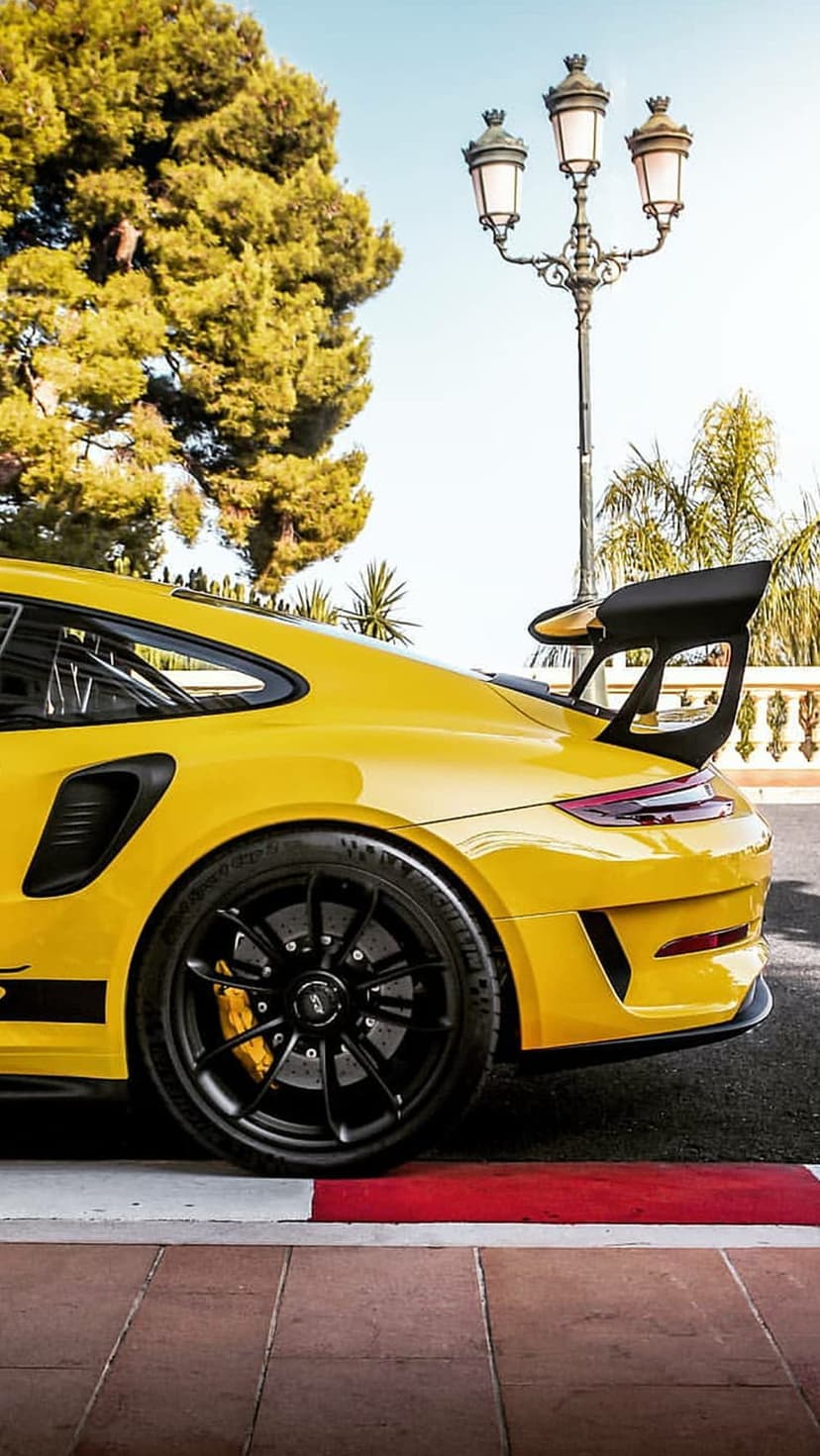 Yellow Porsche 911 GT3 RS with a massive black wing parked on a race track alongside red and white kerbs.