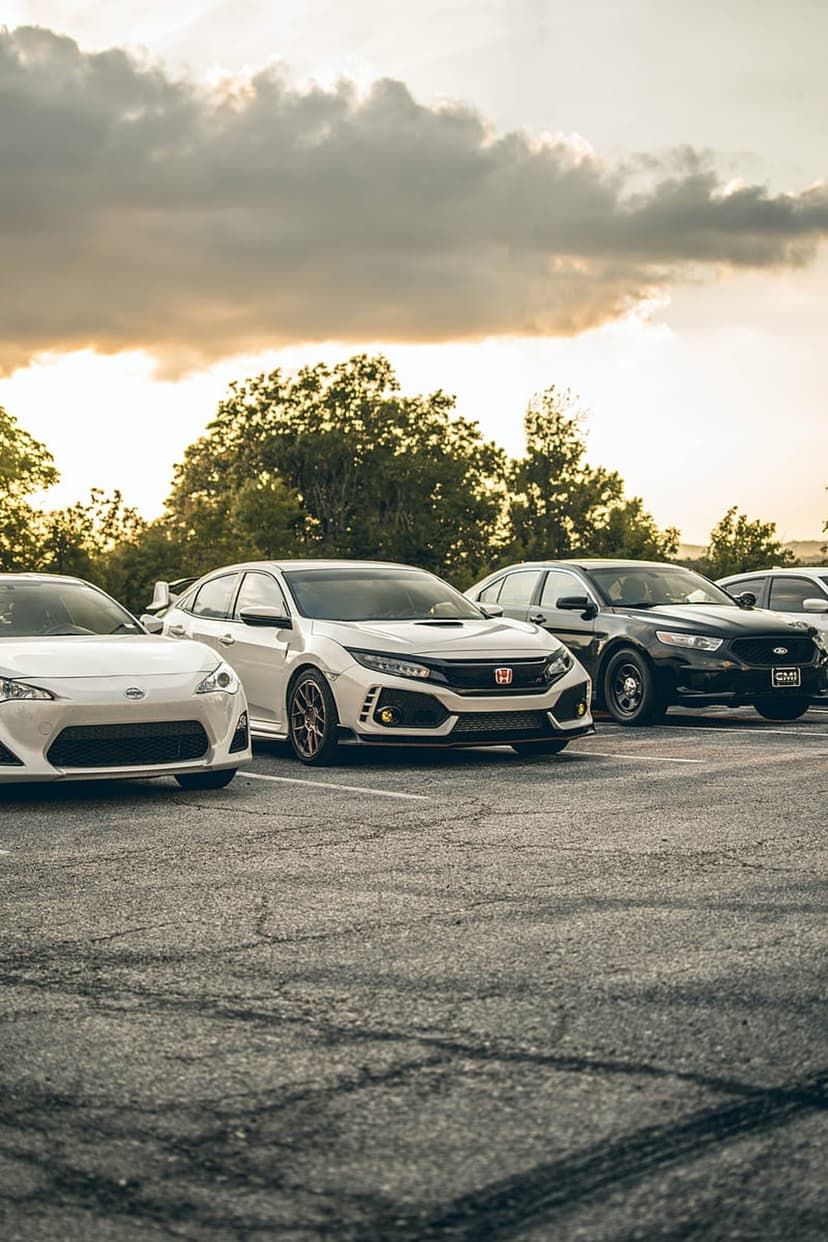Sleek white and black cars parked on asphalt beneath a dramatic sunset sky filled with dark, heavy storm clouds.
