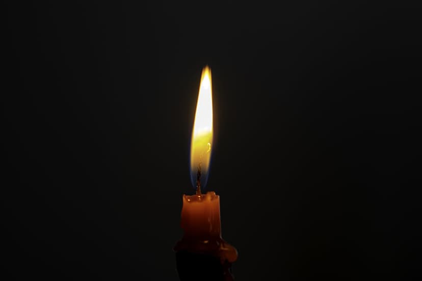 Single candle flame with a blue base and golden tip glows intensely against a pitch-black backdrop with wax drips.