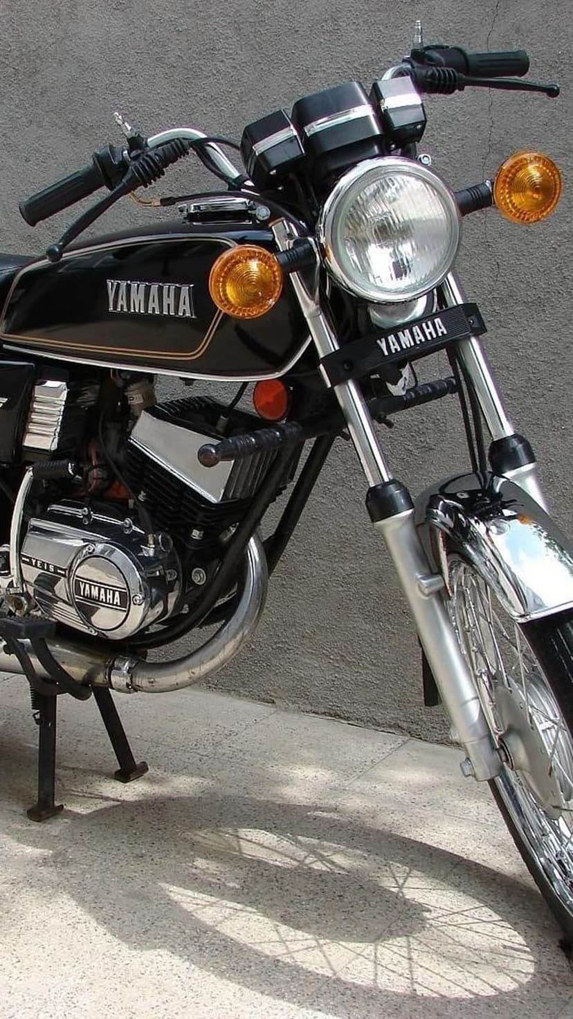 Black Yamaha motorcycle with a round headlight and chrome engine parts parked against a textured grey wall.