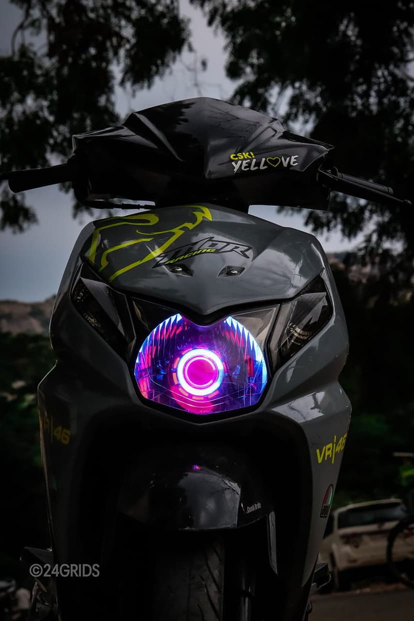 Honda Dio scooter featuring a glowing pink LED headlight and VR46 yellow graphics against a background of trees.