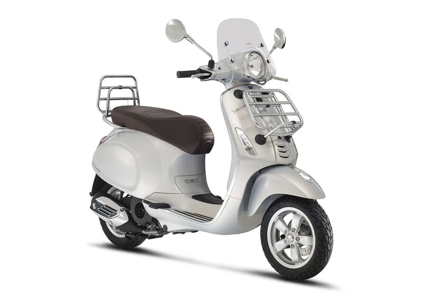Silver Vespa Primavera scooter with a brown seat, chrome racks, and a windshield on a white background.