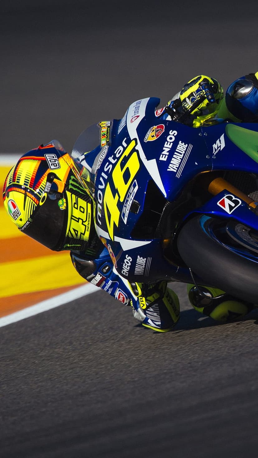 Valentino Rossi leans a blue Yamaha motorcycle into a turn over orange and white track kerbs at high speed.