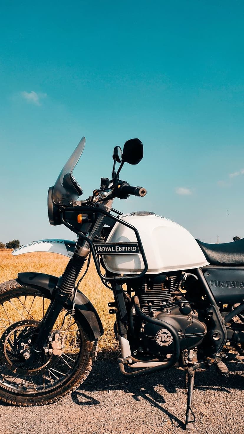 Royal Enfield Himalayan motorcycle parked on a dirt path against a clear blue sky and golden grass fields.
