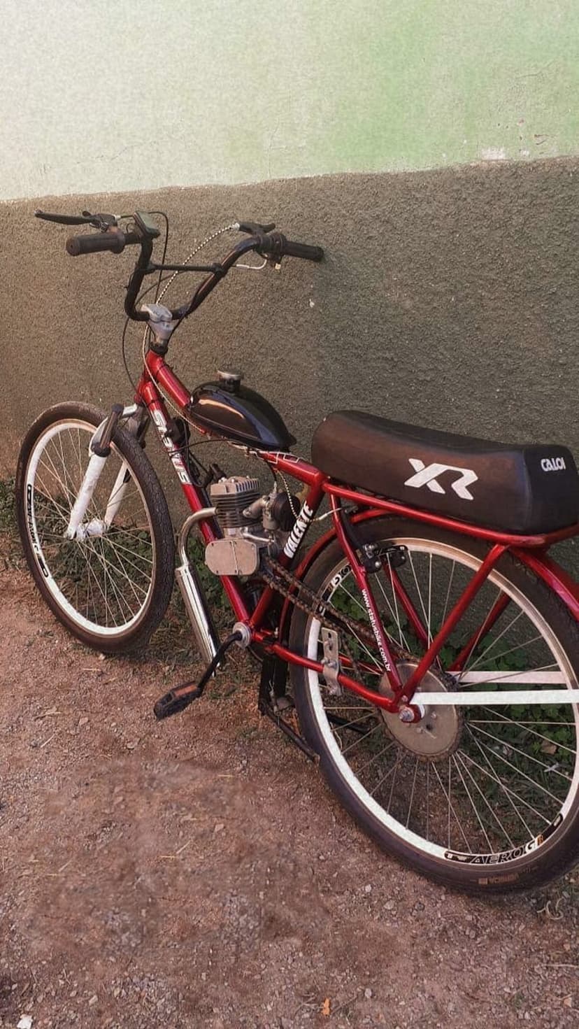 Crimson motorized bicycle with an XR seat and exposed engine, parked against a grey textured stone wall.