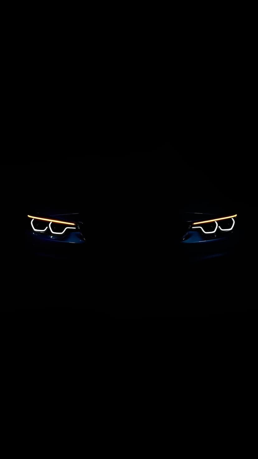 Amber LED car headlights glow intensely against a solid black background in a vertical minimalist composition.