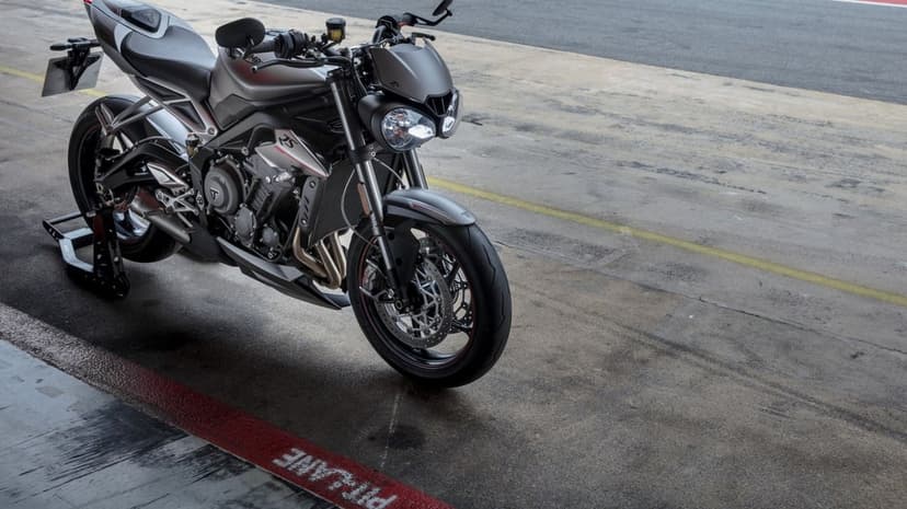 Silver Triumph Street Triple RS motorcycle on a paddock stand in a concrete pit lane with red and yellow lines.