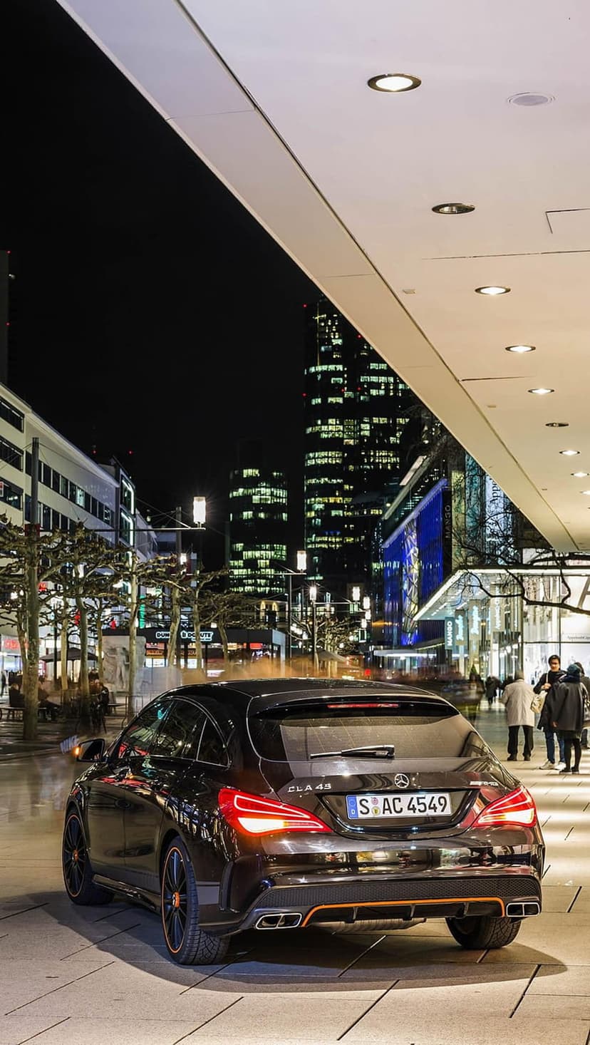 Black Mercedes-AMG CLA 45 car parked on a night city street with glowing red taillights and urban bokeh.